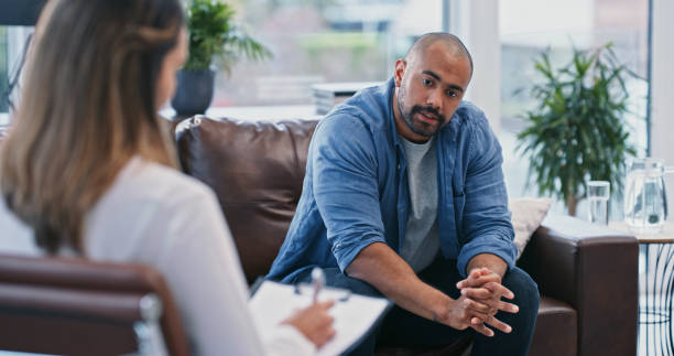 przycięte ujęcie przystojnego młodego mężczyzny wyglądającego na zamyślonego podczas sesji ze swoją terapeutką - mental health professional zdjęcia i obrazy z banku zdjęć