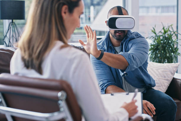 Cropped shot of a young man wearing a vr headset while sitting in session with his female therapist stock photo