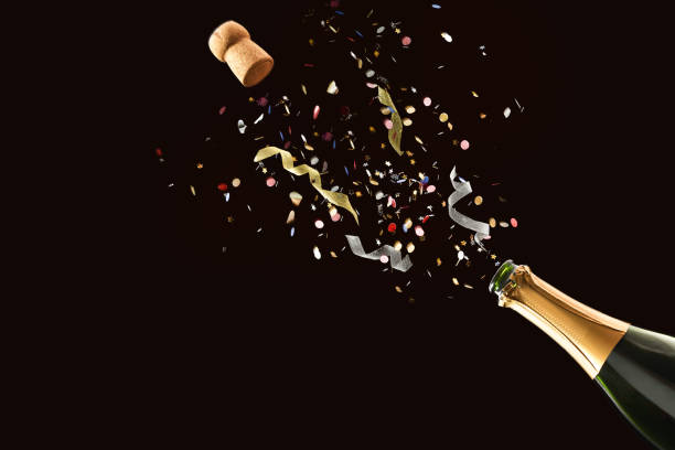 Freshly opened bottle with confetti and ribbons coming out isolated Festive concept with freshly opened bottle of sparkling wine with confetti and ribbons coming out on black isolated background uncork wine stock pictures, royalty-free photos & images