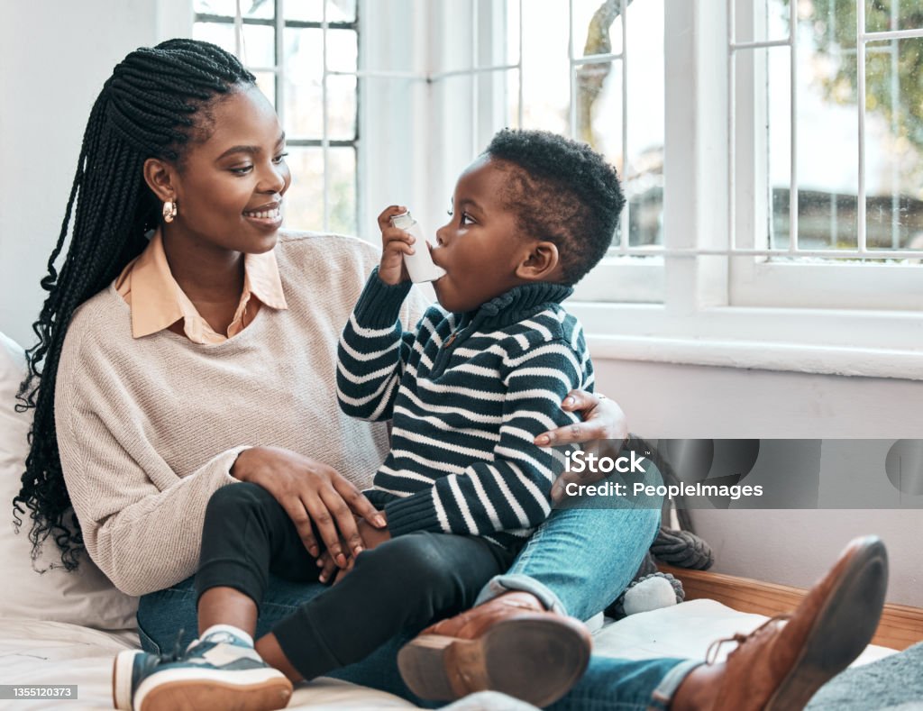 Shot of a little boy using his inhaler while sitting at home with his mother Just like that... Asthmatic Stock Photo