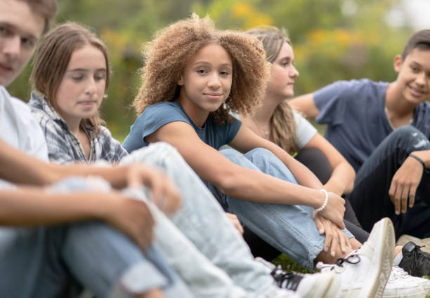 Children sit in a circle on the grass with the teacher and talk after sports activities