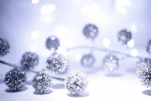 Defocused Christmas background. White, silver, gray blue Christmas background with defocused lights and Christmas geometric blurred balls. White or silver lights on a silver blue background.