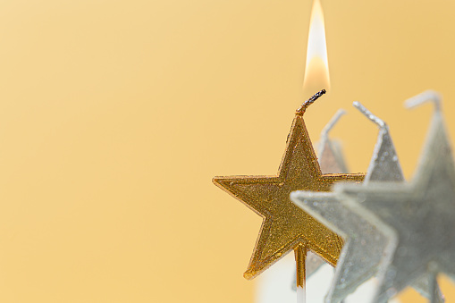 Burning candle in the form of a star on a yellow background