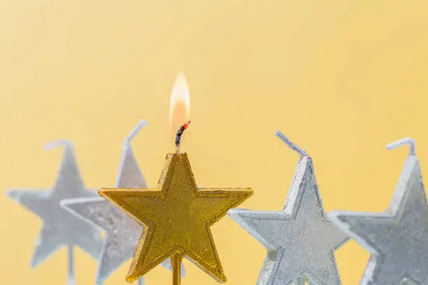 Burning candle in the form of a star on a yellow background, close-up