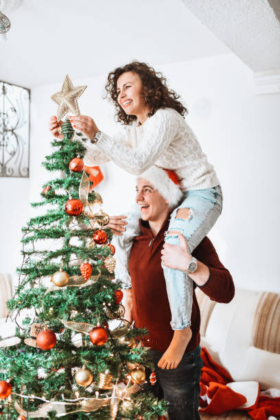 istock Male Carrying Girlfriend On Shoulders While Decorating Christmas Tree 1355129907