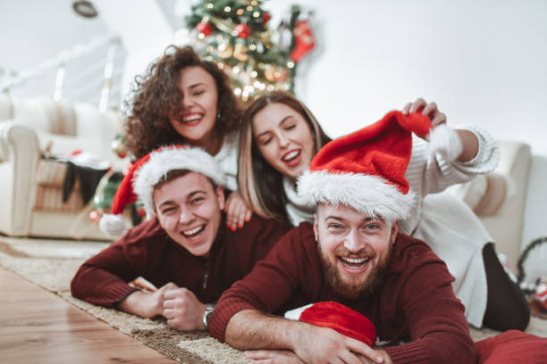 istock Happy Couples Enjoying Taking Christmas Selfies With Santa Hats Under Tree 1355130215