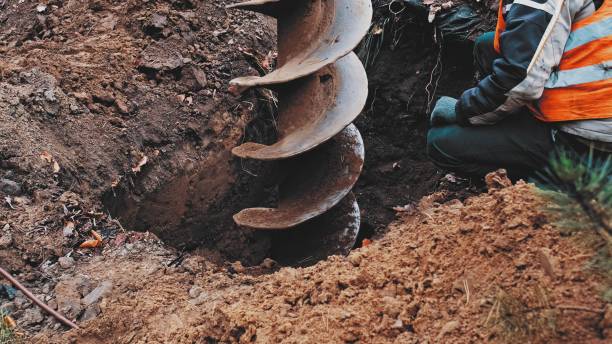 Skilled Construction Worker in Protective Vest Overseeing Big Earthworks Machine Drill Excavating Ground