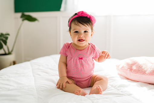 Adorable little baby sitting up in bed and laughing with her mom. Cute infant baby feeling happy in the bedroom