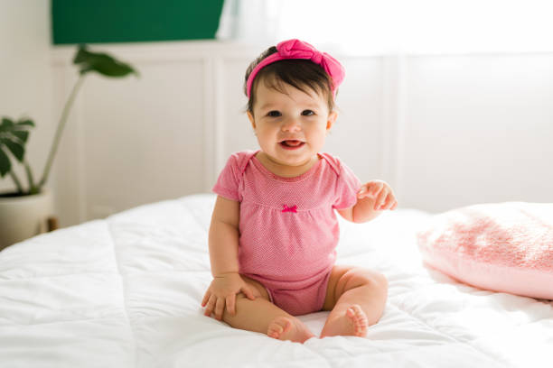 Beautiful baby smiling and making eye contact Adorable little baby sitting up in bed and laughing with her mom. Cute infant baby feeling happy in the bedroom baby girls stock pictures, royalty-free photos & images