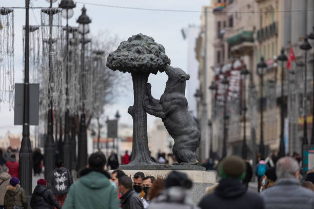 Madrid, Spain - Dec 27, 2020: The famous statue of the bear and the strawberry tree, in Puerta del Sol, surrounded by dozens of people on a cold winter afternoon