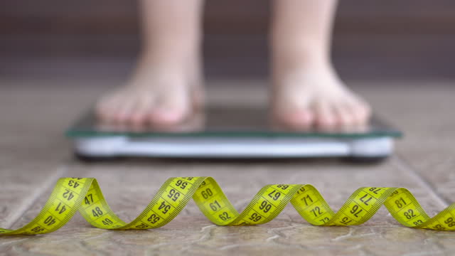 Woman feet standing on weigh scales. A tape measure in the foreground. Dieting