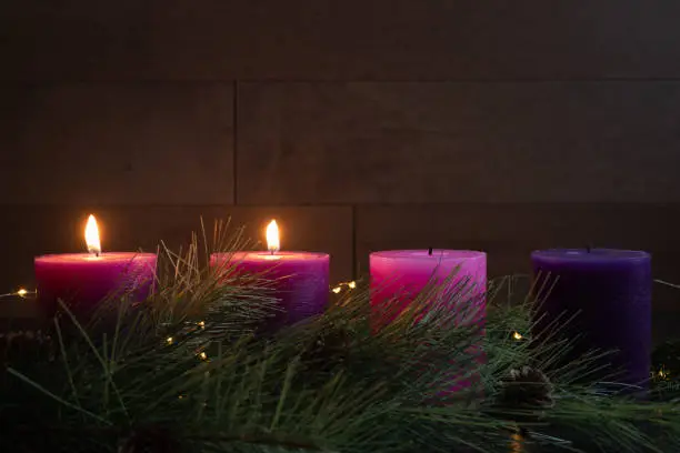 Photo of Two advent pillar candles burning against wood background