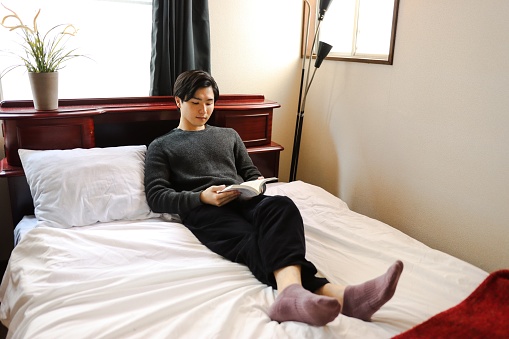 Young man wearing glasses is reading a book on the bed before going to bed at night