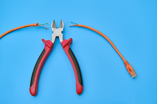 Cutting a computer network wire with wire cutters, blue studio background