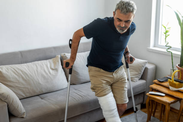 istock Man with broken leg trying to get up from sofa 1355137469