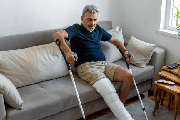 istock Man with broken leg trying to get up from sofa 1355137509