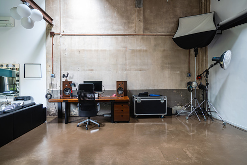 Interior shot of an industrial loft of a photographer. Flashes and tripods in the corner. A desktop with computers in the center.