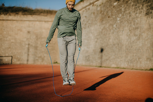 Fitness, sport, people, exercising and lifestyle concept - man skipping with jump rope outdoors