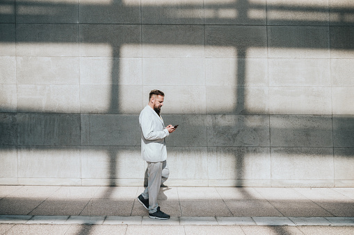 elegant bearded senior business man standing in city in front of wall and looking at mobile