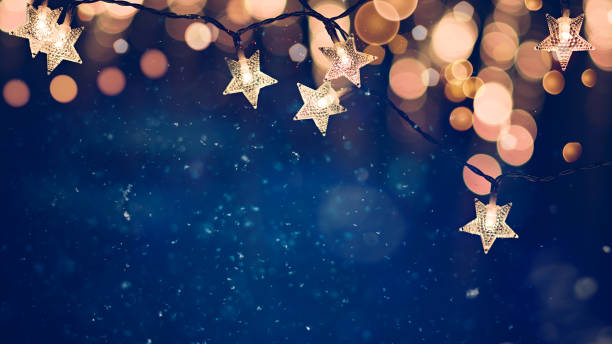 guirlandes lumineuses de noël en forme d’étoile sur fond de nuit bleue avec des lumières bokeh dorées - christmas lights christmas lighting equipment holiday photos et images de collection
