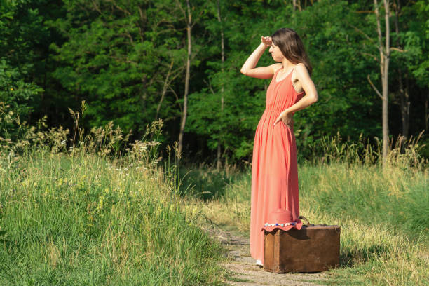 istock Woman standing in forest road with old suitcase 1355147558