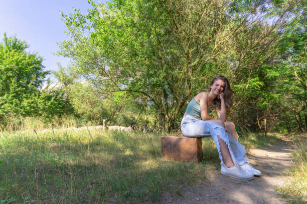 Fair-haired girl in casual clothes resting on a log on a woodland footpath.