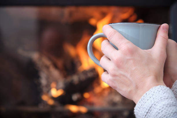 istock Woman hands holding a cup in front of a fireplace 1355147849