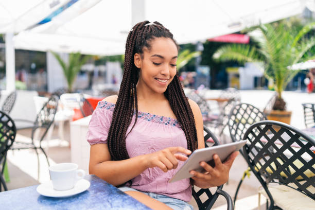 istock Smiling afro woman drinking coffee in cafeteria and using digital tablet 1355150418