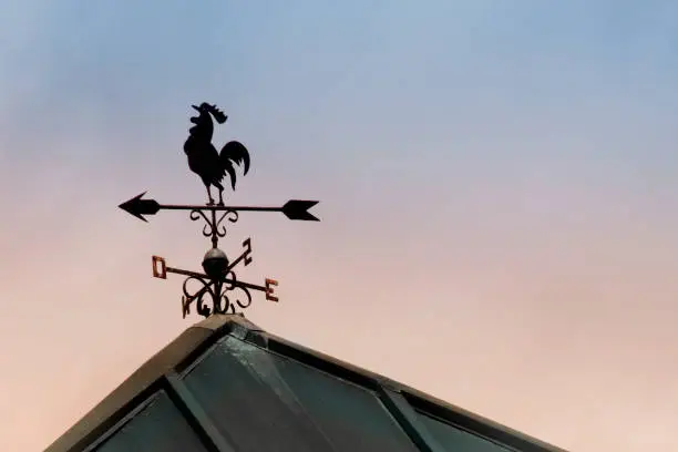 Close up of weathervane in rooster shape silhouetted on a rooftop, sunset sky in the background with copy space on the right.  Tui, Pontevedra province, Galicia, Spain.
