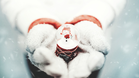 girl wearing gloves on a snowy winter day, holding a snow globe