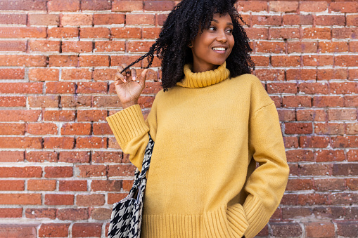 Portrait of pensive, smiling young African American woman wearing yellow sweater looking away. Copy space. Lifestyle concept.