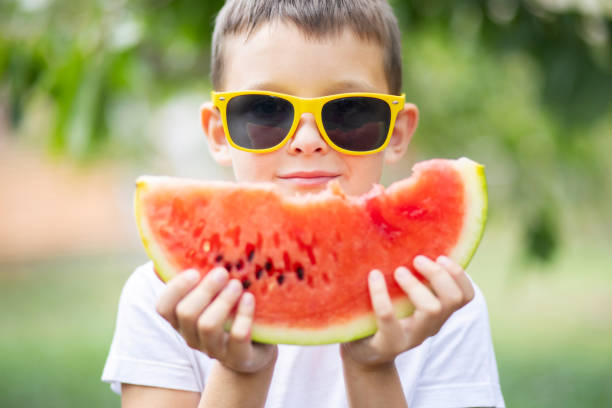 Cute boy in yellow sunglasses eating watermelon outdoors in summer. Healthy eating seasonal berries and fruits Cute boy in yellow sunglasses eating watermelon outdoors in summer. Healthy eating seasonal berries and fruits. yellow melons field stock pictures, royalty-free photos & images