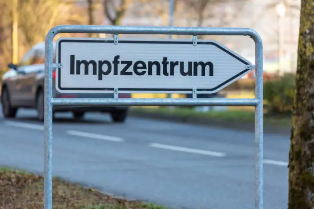 outdoor sign with the german word Impfzentrum, car on street in background