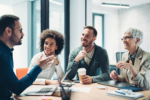 Portrait of handsome smiling businessman with his colleagues during a meeting in office board room. Successful team leader and his team working in background.