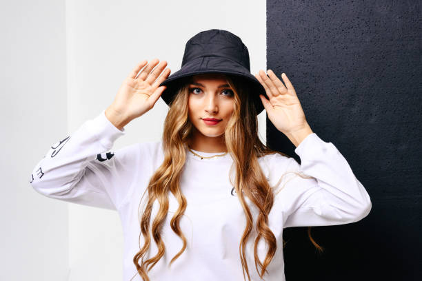 The beautiful young girl in a white T-shirt, black hat with gray-blue eyes and long hair on a black and white background. stock photo