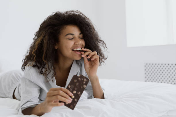 Mixed race woman eating milk chocolate in bed