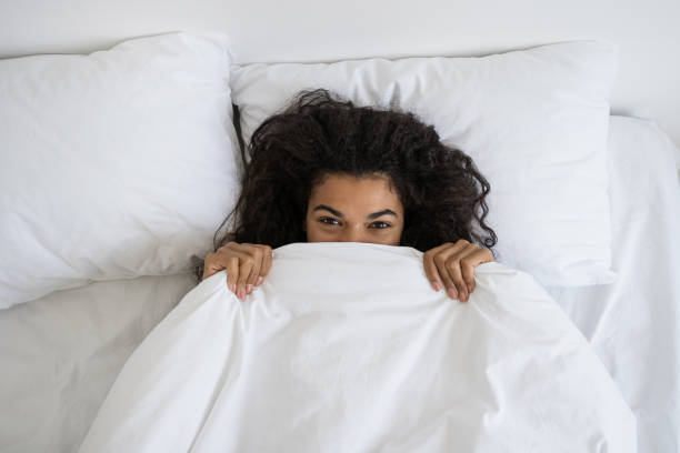 istock Afro american woman hides under soft white blanket 1355162221