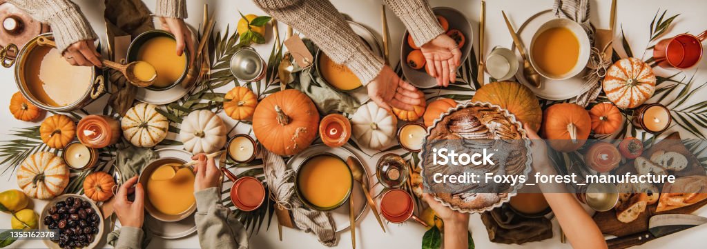People eating over fall festive table set, top view Autumn table set for Thanksgiving day celebration or gathering dinner. Flat-lay of people eating and celebrating over table with pumpkin soup, charcuterie board, apple pie and candles, top view People Stock Photo