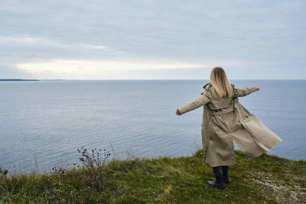 das mädchen steht am rande einer klippe und schaut auf das meer oder meer. die frau schaut in die ferne. erstaunliche malerische aussicht auf die natur. schöne felsen und meer. harmonie, entspannender lebensstil. reisen, abenteuer - cliff at the edge of grass sea stock-fotos und bilder