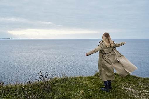 Girl stands on the edge of a cliff and looks at the ocean or sea. The woman looks into the distance. Amazing scenic nature view. Beautiful rocks and sea. Harmony, relaxing lifestyle. Travel, adventure