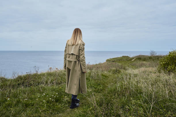 das mädchen steht am rande einer klippe und schaut auf das meer oder meer. die frau schaut in die ferne. erstaunliche malerische aussicht auf die natur. schöne felsen und meer. harmonie, entspannender lebensstil. reisen, abenteuer - cliff at the edge of grass sea stock-fotos und bilder