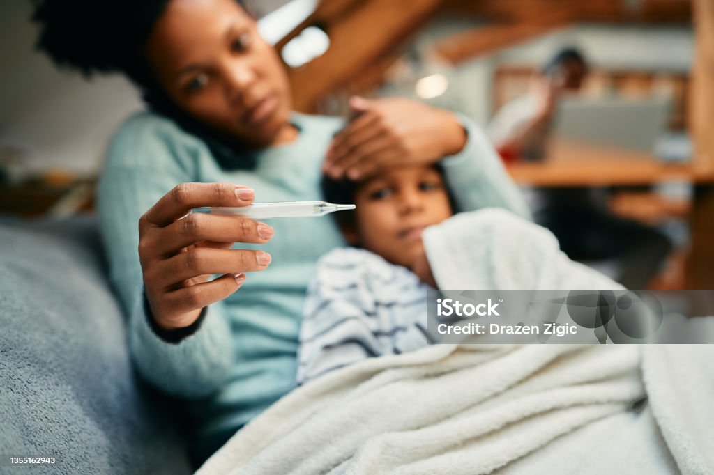 Close-up of black mother measuring sick son's temperature. Close-up of African American mother using thermometer and measuring temperature or her sick son at home. Child Stock Photo