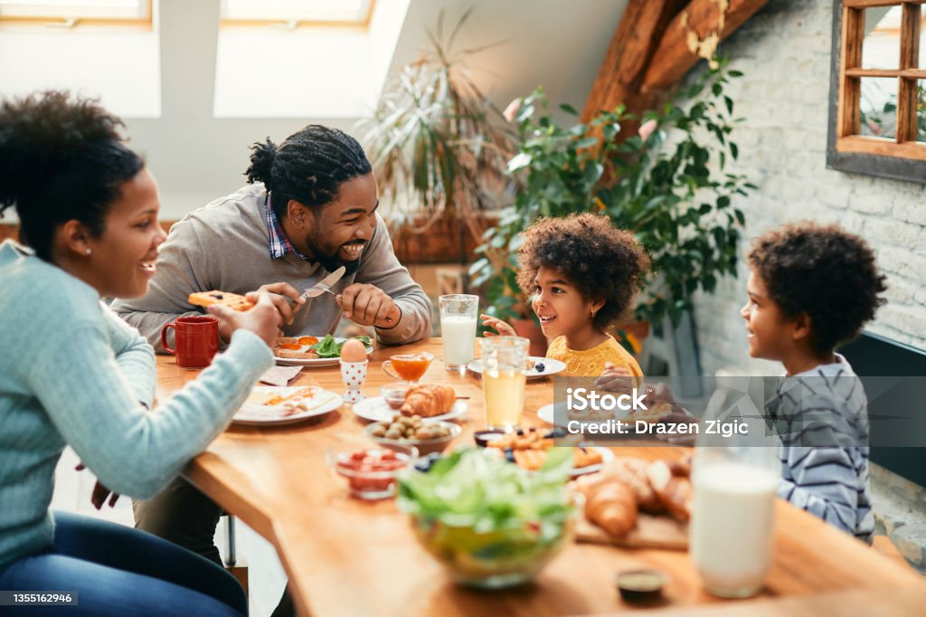 Happy African American family enjoying in conversation while eating breakfast together at dining table. Happy black parents and their kids talking while having breakfast together in dining room. Family Stock Photo