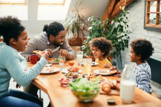 Photo of Happy African American family enjoying in conversation while eating breakfast together at dining table.