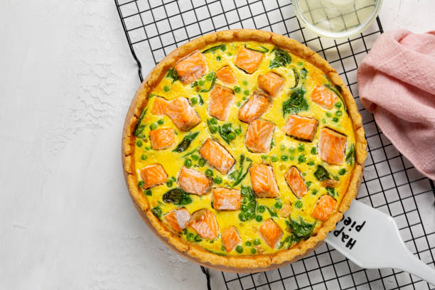 istock Quiche or pie with salmon, spinach, green peas, eggs and cheese on a white concrete  table. Directly above. 1355164124