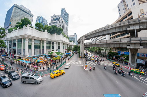 Wide angle view of Ratchaprasong Junction. Showing traffic and the BTS elevated railway. The Erawan Shrine, formally known as the Thao Maha Phrom Shrine, is visible in the bottom left corner, with tourist and worshipers in attendance.