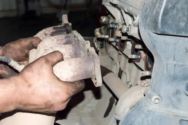 Photo of The mechanic removes the exhaust manifold from the car engine