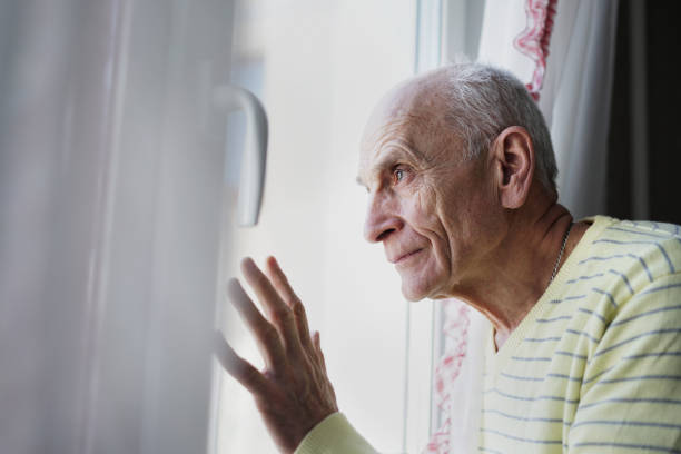 istock Mature person looking through window with white curtain at home 1355165472
