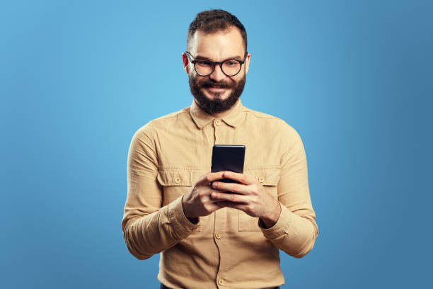 istock Man smiling and using smartphone, standing isolated over blue background 1355168658