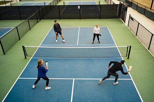 A group of young adults playing Pickleball on an outdoor court.